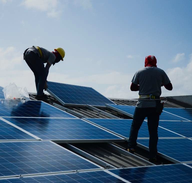 Two men installing a solar panel on a rooftop in Jaipur, showcasing renewable energy efforts in the region.